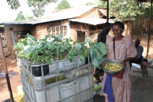 Deborah Gita poses next to her aquaponics farming system where she just harvested kale and beans. Aquaponics farming project beneficiaries are already reaping from their systems